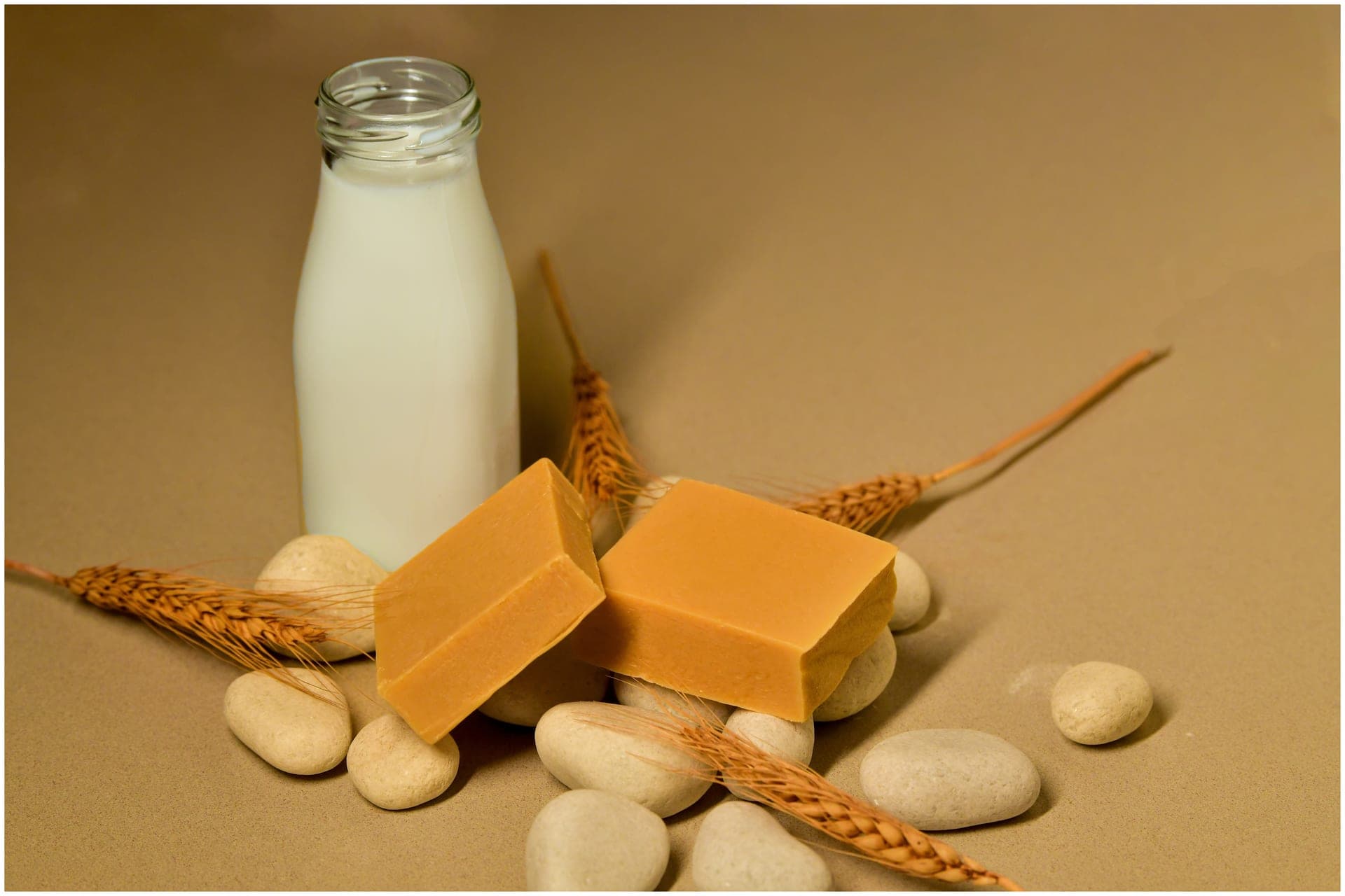 Goat milk soap beside a glass milk bottle and wheat